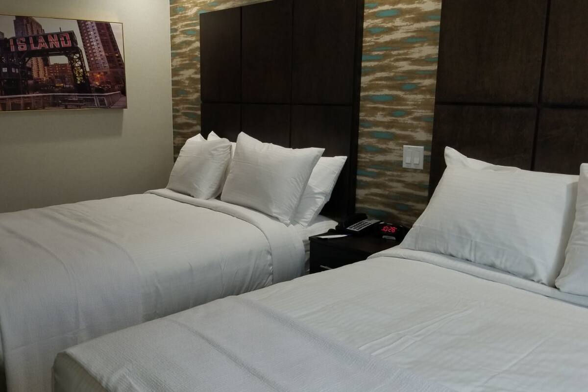 Ein Hotelzimmer mit zwei Einzelbetten, einem Nachttisch mit Telefon und einem an der Wand hängenden Stadtbild.