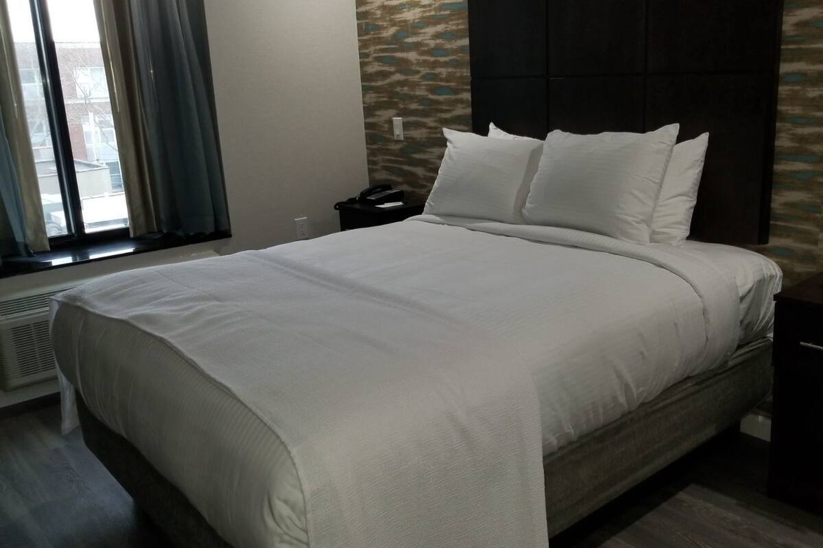Ein modernes Hotelzimmer mit einem großen Bett, einem Nachttisch, einem Heizgerät und einem kleinen Schreibtisch mit einer Uhr.