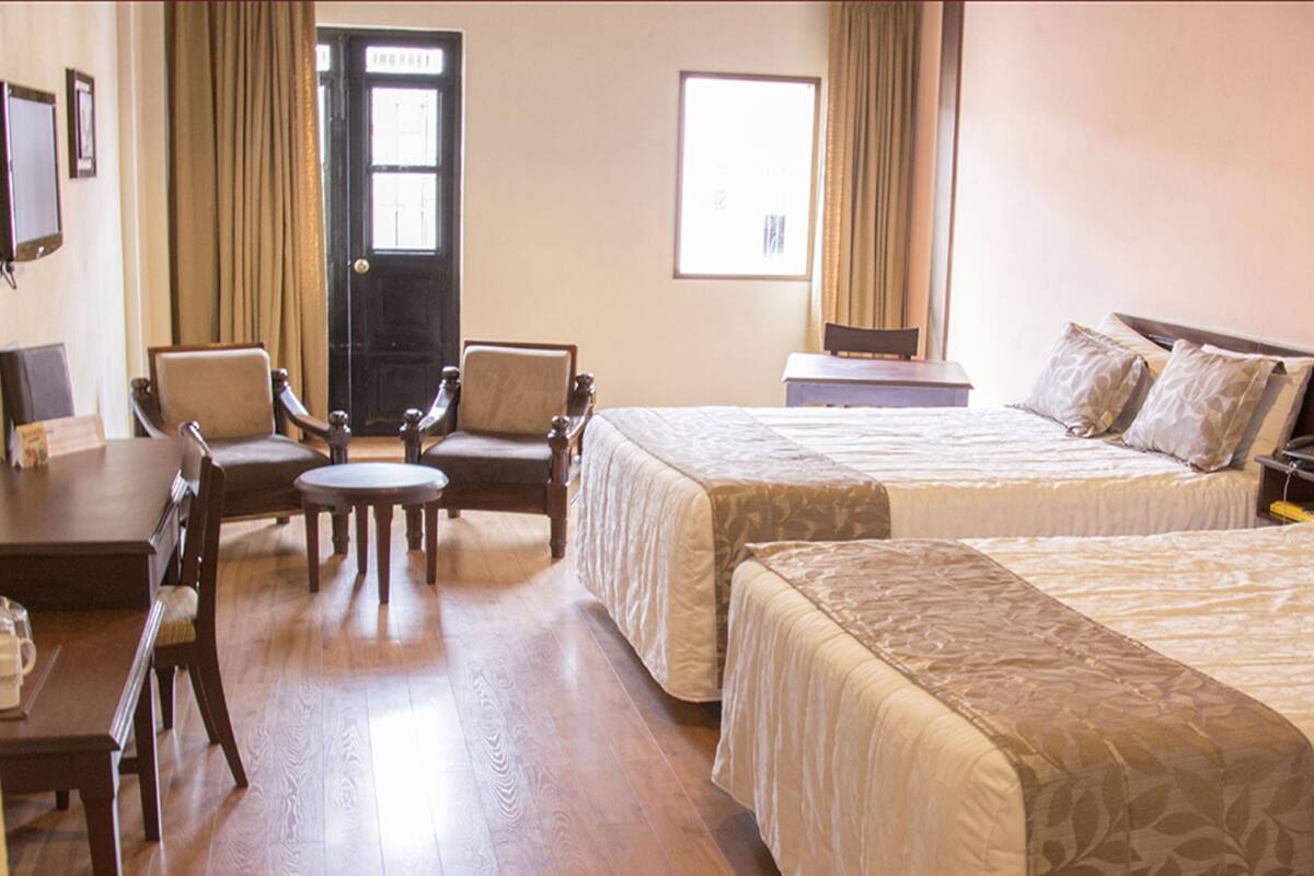 A hotel room with two beds, a desk, a chair, and a small table.