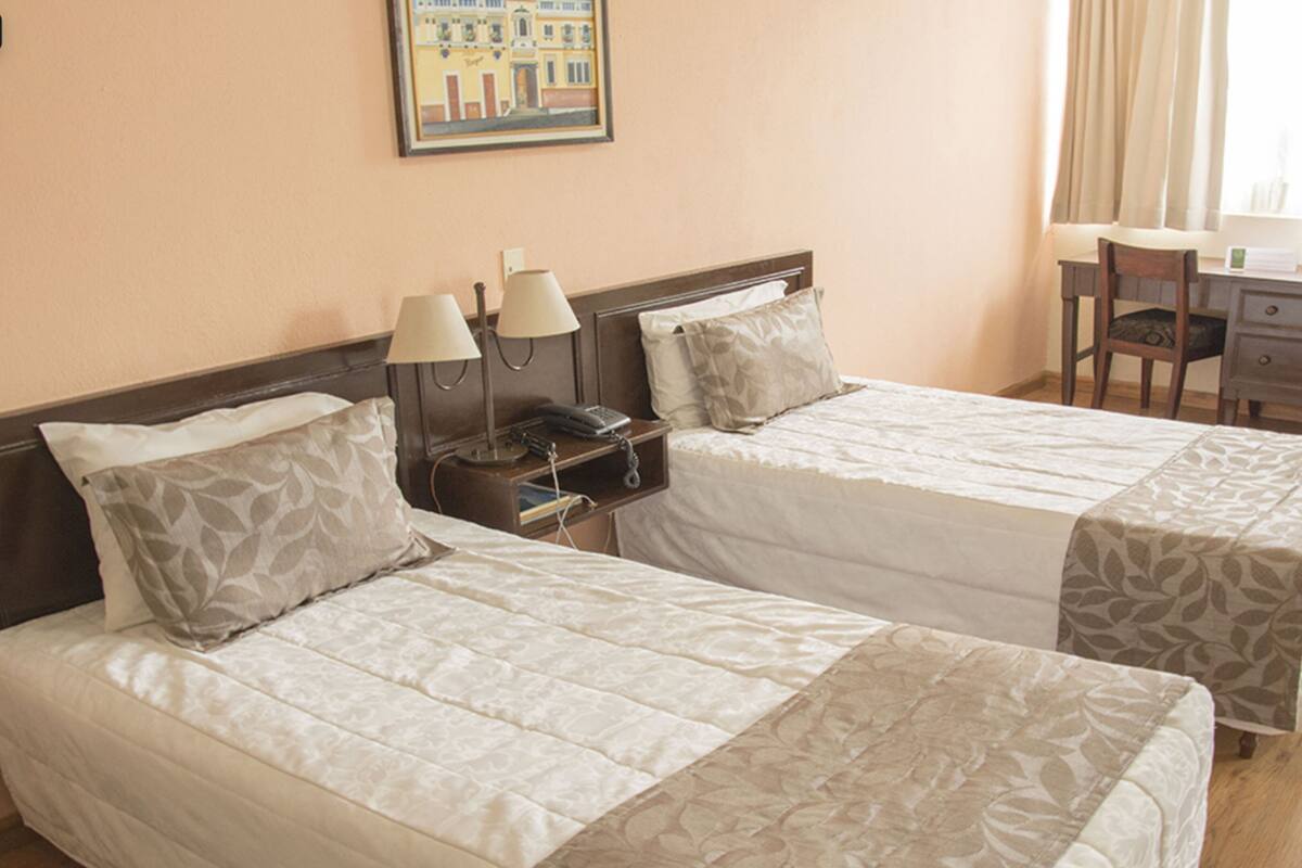 A hotel room with two beds, a desk, a chair, and a nightstand with lamps.