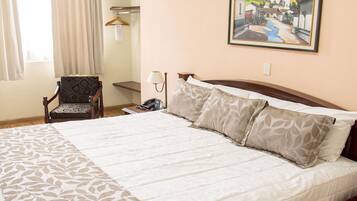 A hotel room with a large bed, a chair, a painting on the wall, and a window with curtains.
