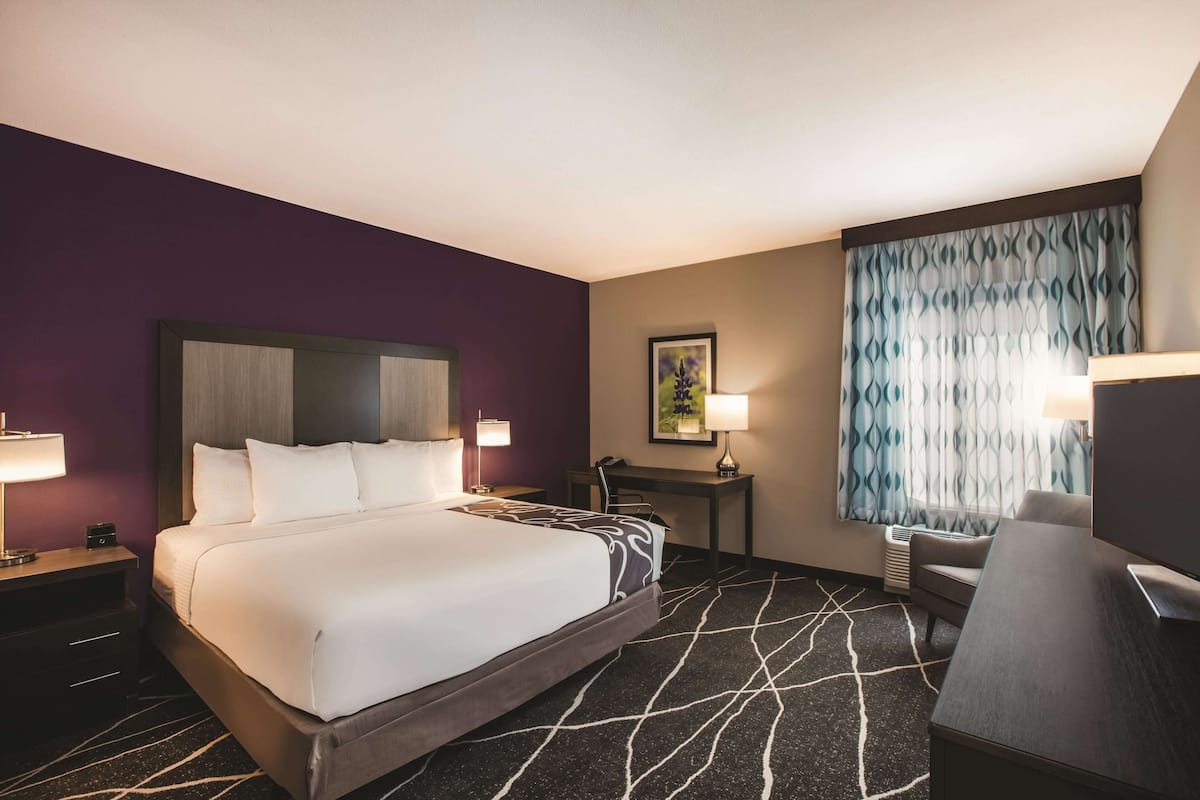 A hotel room with a large bed, a desk, a chair, and a television.