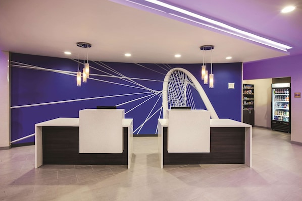 A reception area with two white reception desks, a large wall mural, and a vending machine in the background.