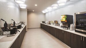 Una cocina moderna con una encimera amplia, máquina para gofres, cafetera y dispensador de fruta.