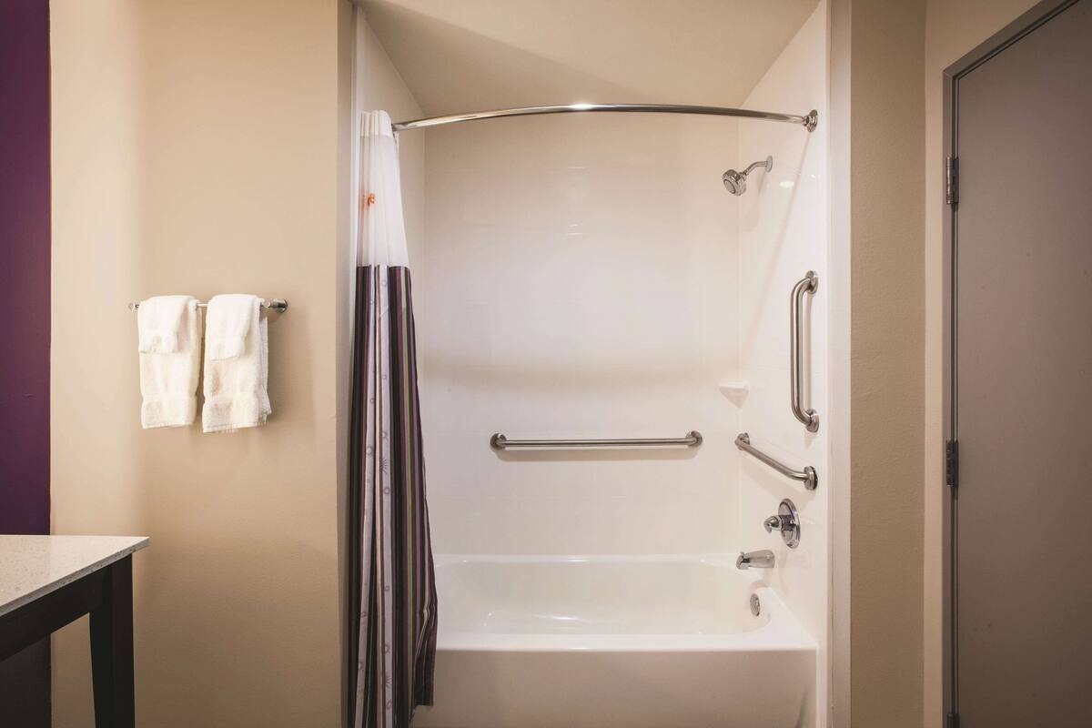 A bathroom with a bathtub, grab bars, and a shower curtain.