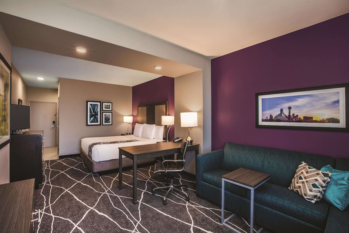 A hotel room with a bed, desk, chair, and a green sofa.