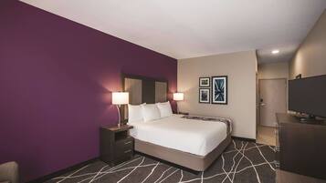 A hotel room with a large bed, two bedside tables with lamps, a TV, and a door leading to another room.