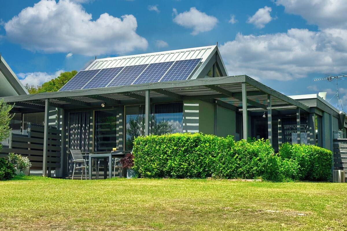 Una casa moderna con paneles solares, un porche cubierto y un césped cuidado.