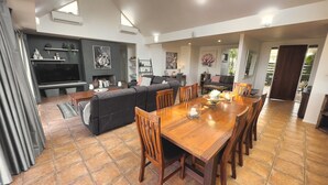 A modern living room with a large TV, dark sofas, a dining table with chairs, and a fireplace. - Grapevines Boutique Accommodation (Pokolbin)