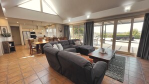 A modern living room with a sectional sofa, dining area, and large sliding glass doors leading to an outdoor patio. - Grapevines Boutique Accommodation (Pokolbin)