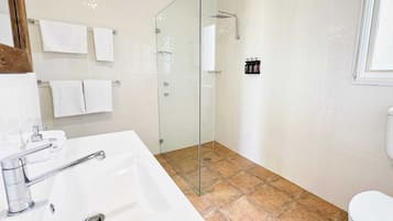 Un baño con lavamanos blanco, cabina de ducha con mampara de vidrio y retrete.