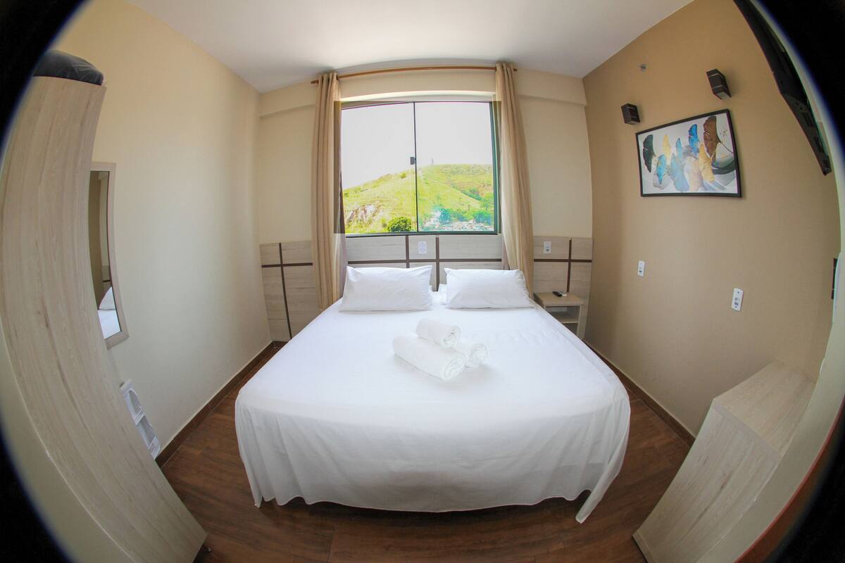 Una habitación con una cama grande, una ventana con cortinas, un cuadro en la pared y suelo de madera.