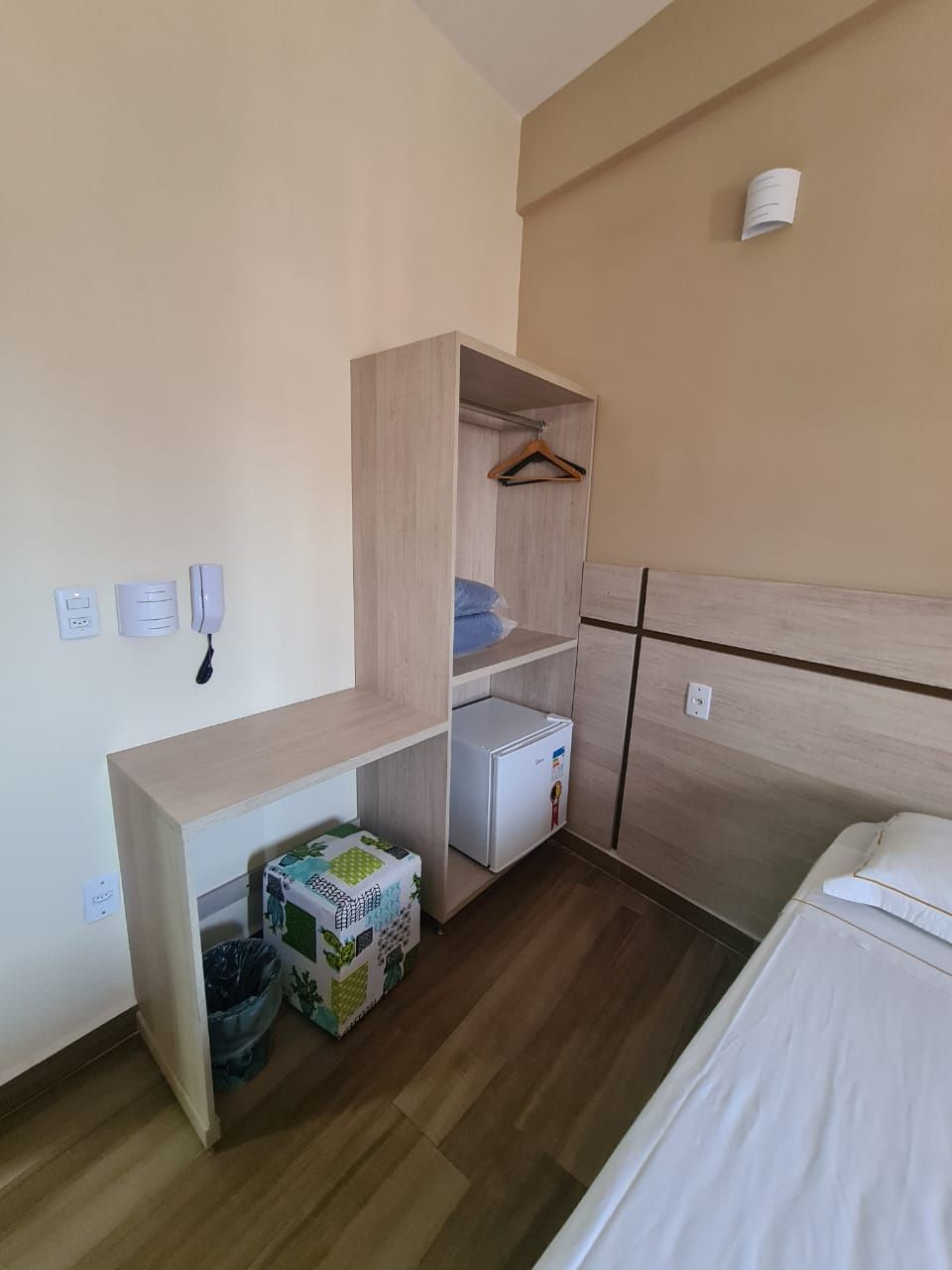 A compact hotel room with a bed, a small desk, a wardrobe, and a trash bin.