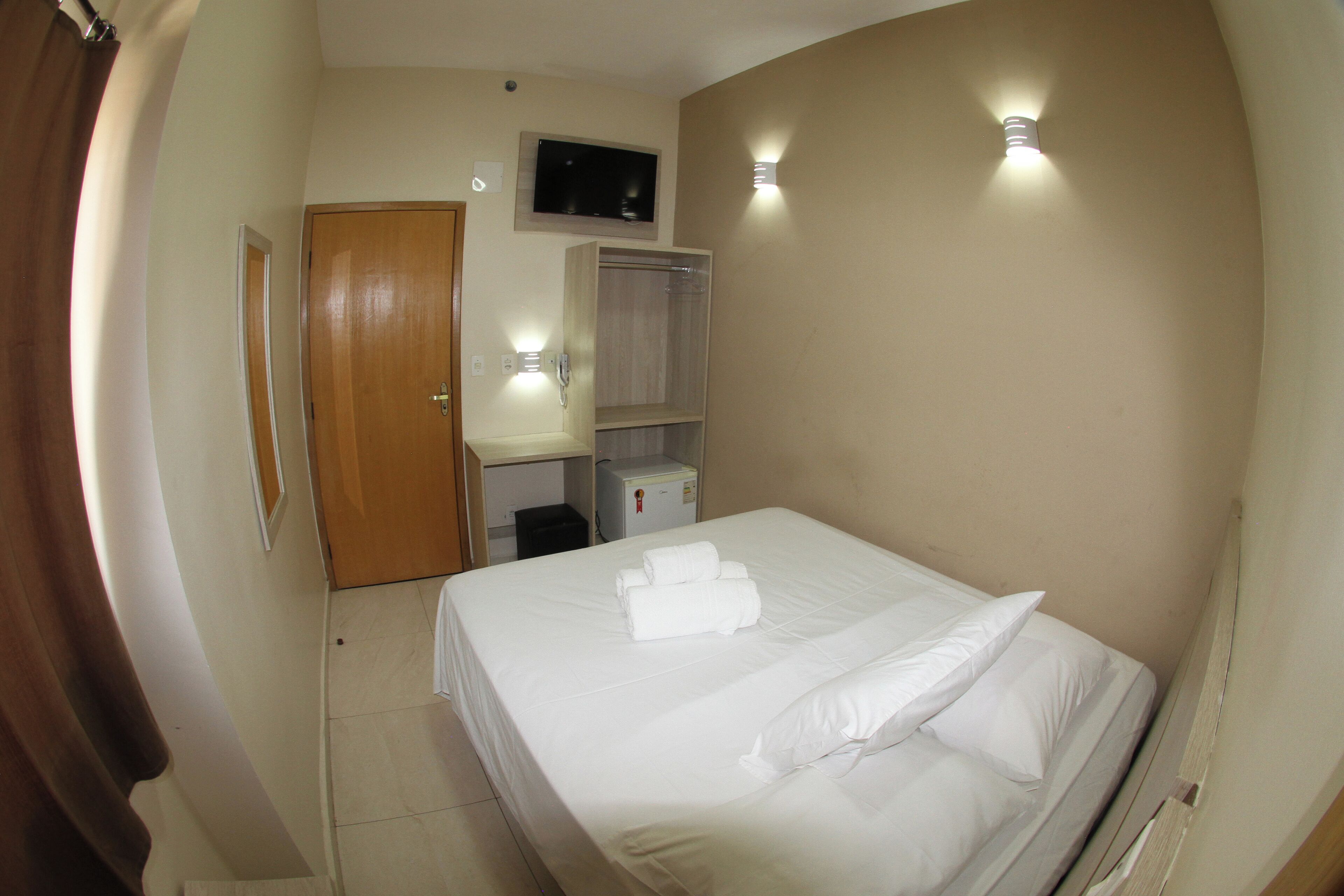 Una camera d'albergo con un letto, una televisione, un guardaroba e una scrivania con una sedia.