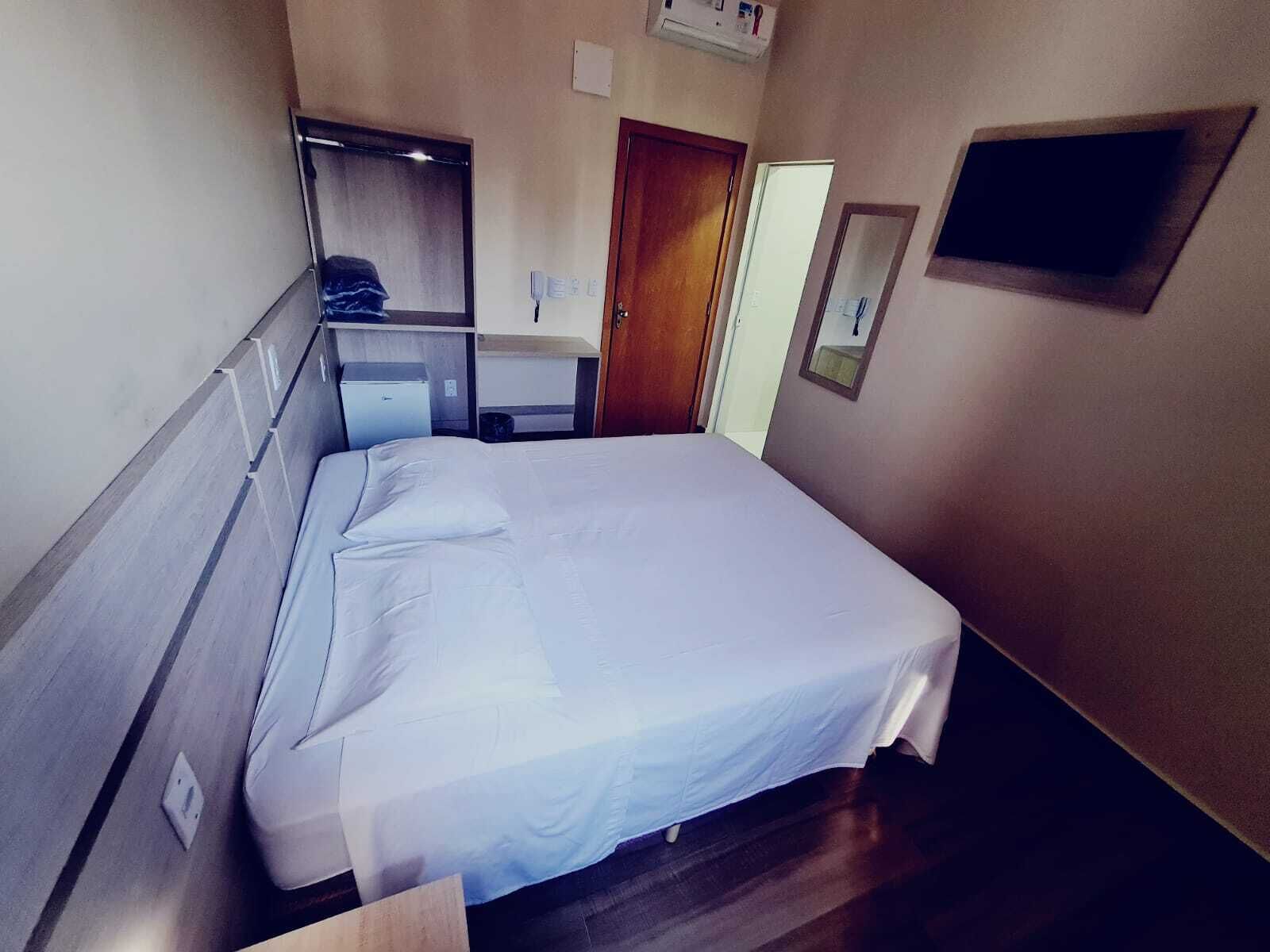 Habitación de hotel con cama, escritorio, silla, espejo, armario y un televisor pequeño.