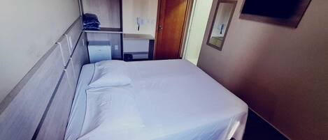Habitación de hotel con cama, escritorio, silla, espejo, armario y un televisor pequeño.