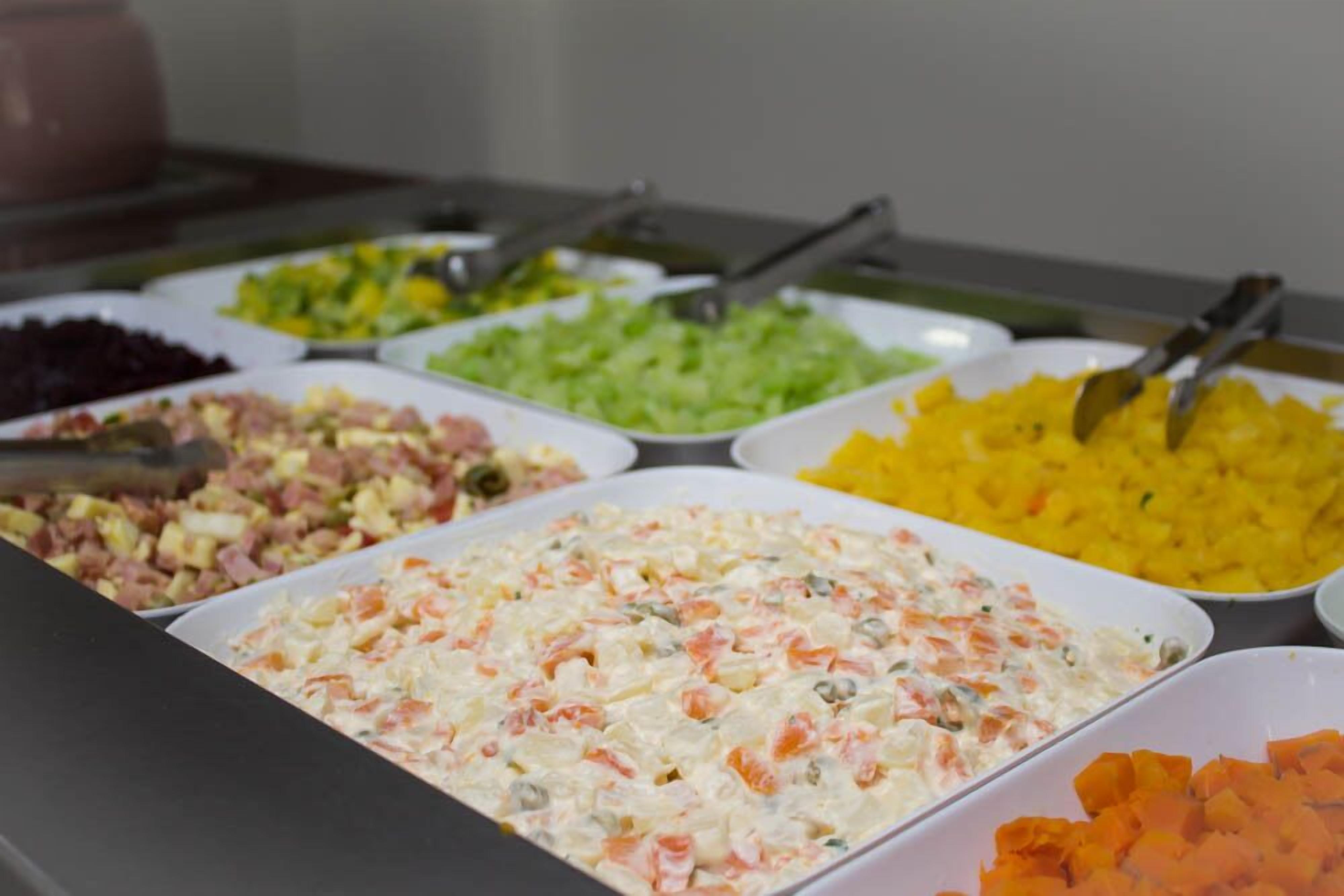 Un buffet proposant divers plats, notamment des salades, une salade de pommes de terre crémeuse et des légumes coupés en dés.