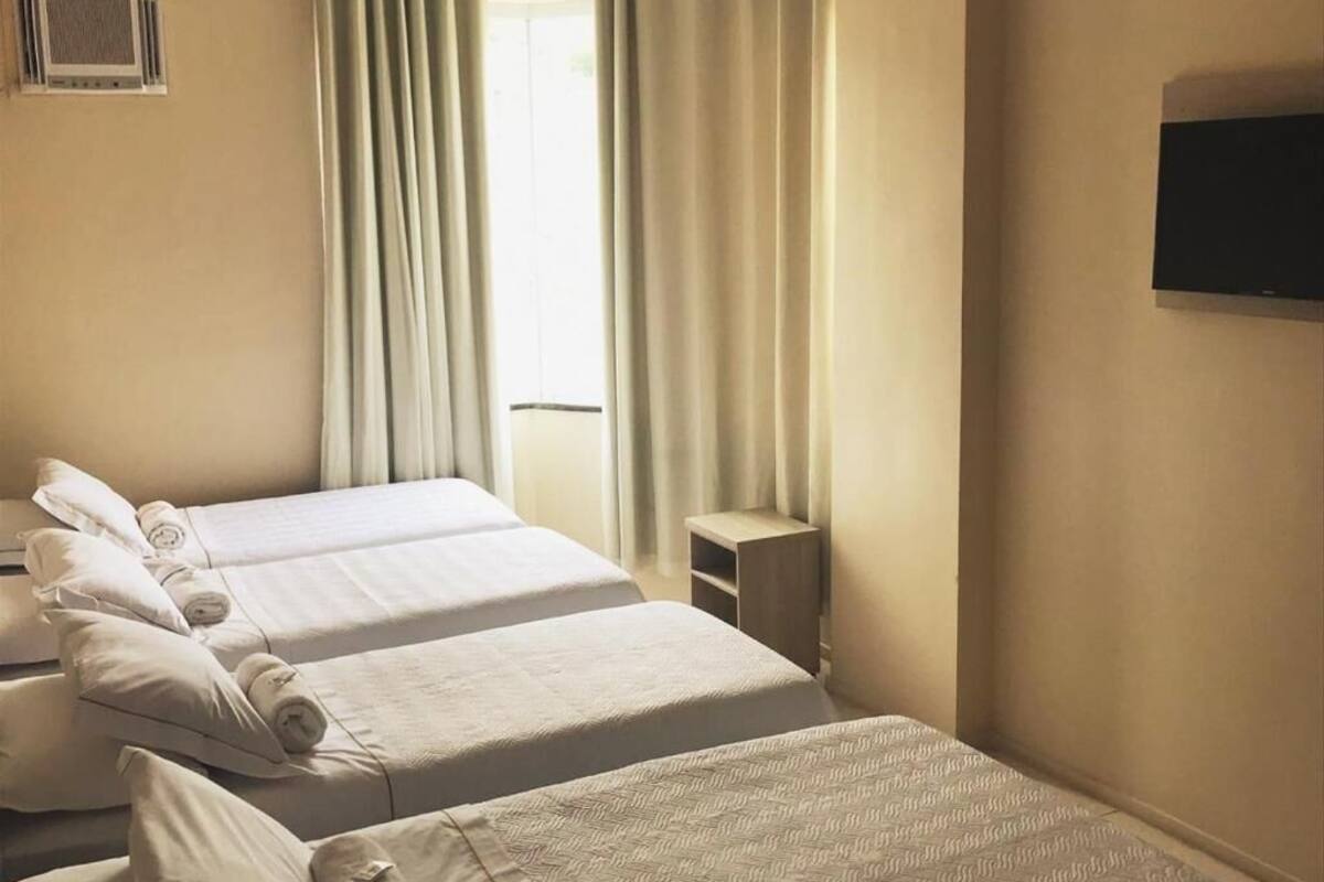 Una habitación de hotel con dos camas, un televisor en la pared y una ventana con cortinas.