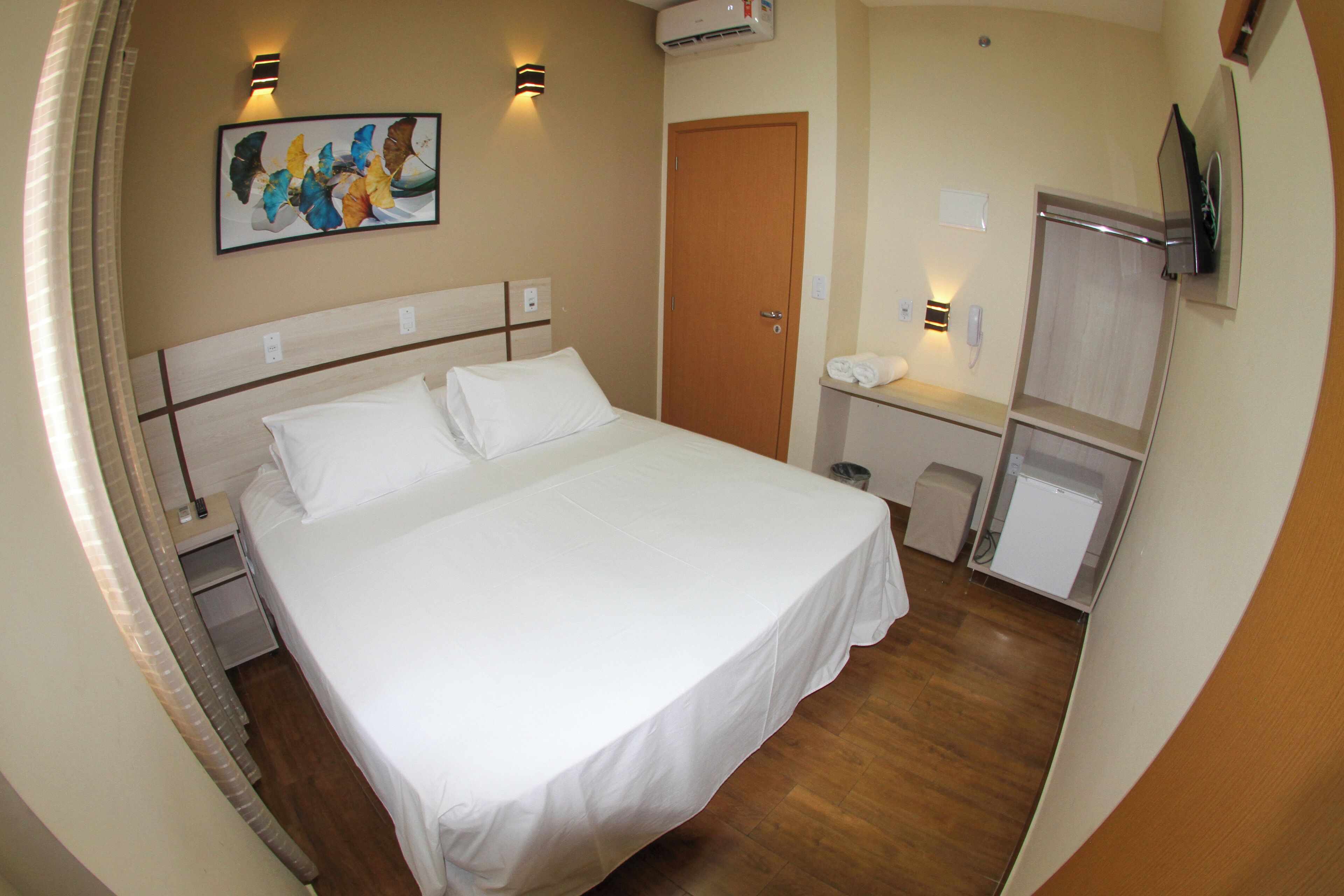 Quarto de hotel com cama, mesas de cabeceira, espelho, televisão e um quadro na parede.