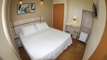 Habitación de hotel con cama, mesitas de noche, espejo, televisión y un cuadro en la pared.
