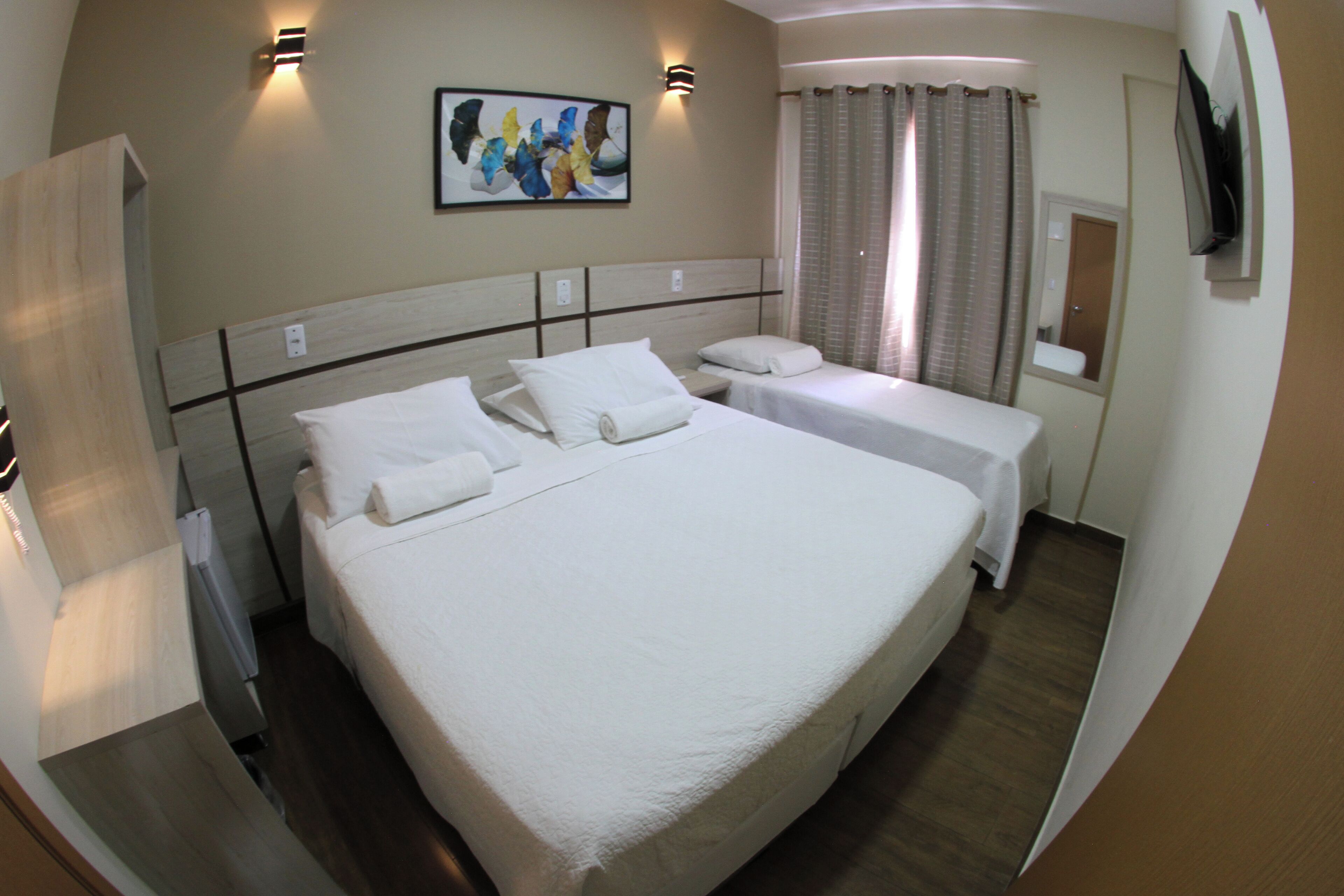 A hotel room with a large bed, two bedside tables, a flat-screen TV, and a painting on the wall.
