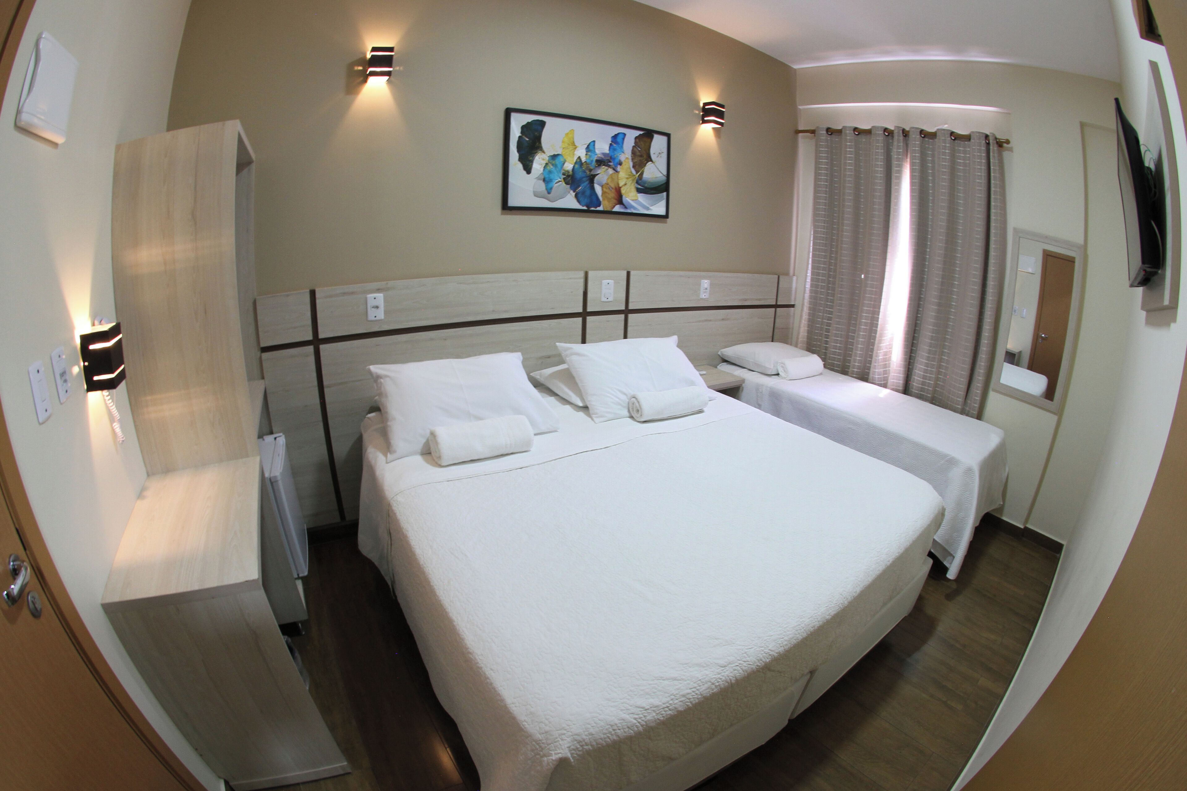 A hotel room with a large bed, two smaller beds, a wardrobe, a painting on the wall, and a shower area.