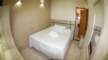 Una cama bien hecha con sábanas y toallas blancas, un cabecero de madera y dos lámparas fijadas a la pared.