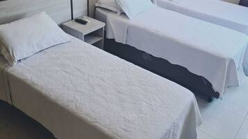 Ein Hotelzimmer mit zwei Einzelbetten, jeweils mit weißer Bettdecke und Kissen. Ein Nachttisch mit Lampe und Telefon steht daneben. Das Zimmer hat ein Holz-Kopfteil und einen Fliesenboden.