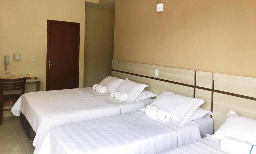 A hotel room with two beds, a wooden headboard, a small table with a chair, and a door.