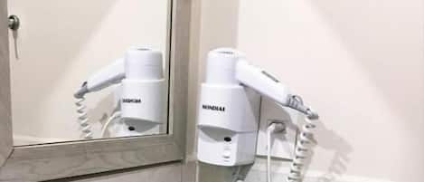 Un baño con un lavamanos blanco, un espejo y un secador de pelo montado en la pared.