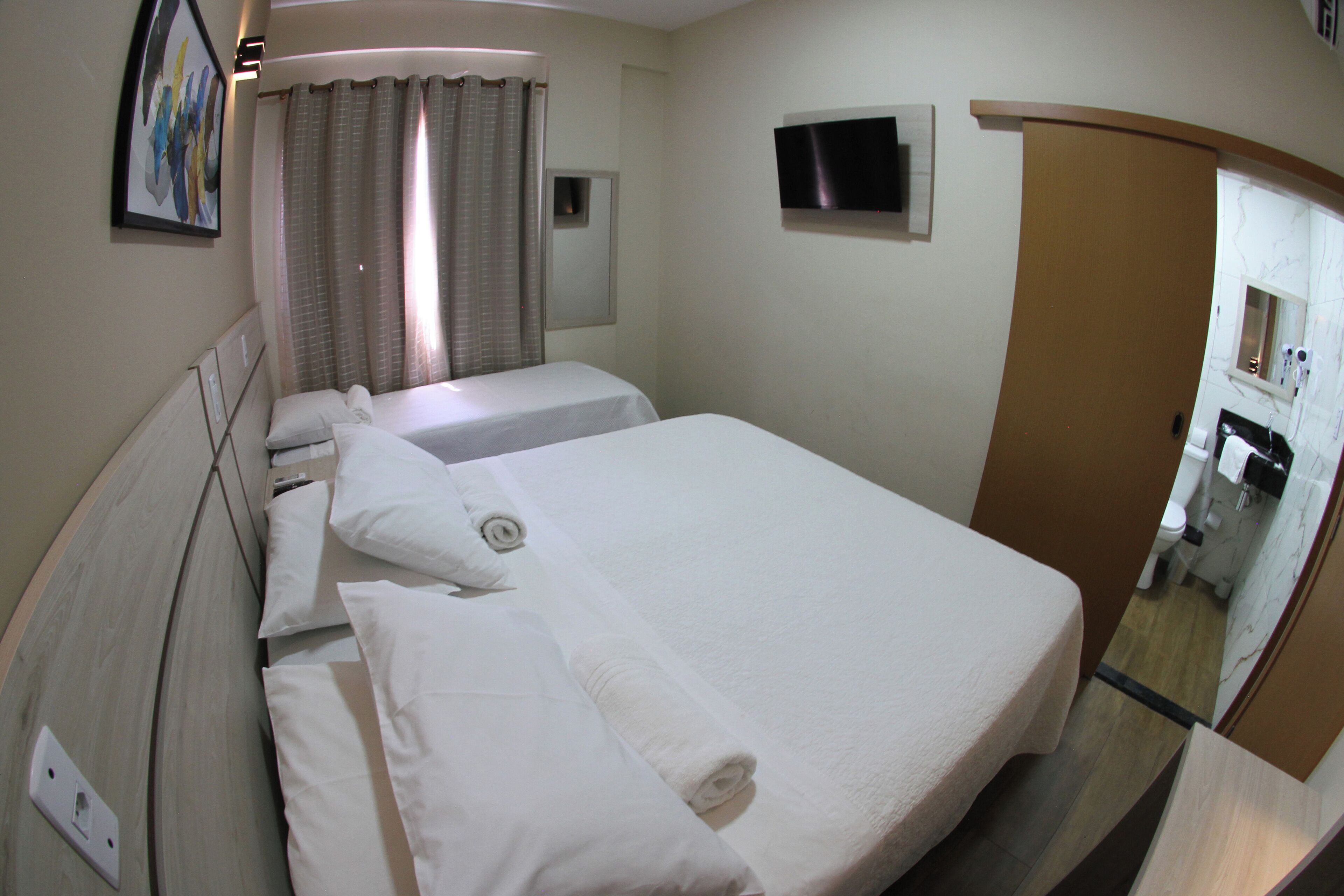 Ein Hotelzimmer mit zwei Betten, einem Fernseher, einem Badezimmer inklusive Spiegel und einem Bild an der Wand.