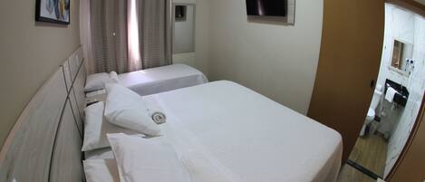 Ein Hotelzimmer mit zwei Betten, einem Fernseher, einem Badezimmer inklusive Spiegel und einem Bild an der Wand.