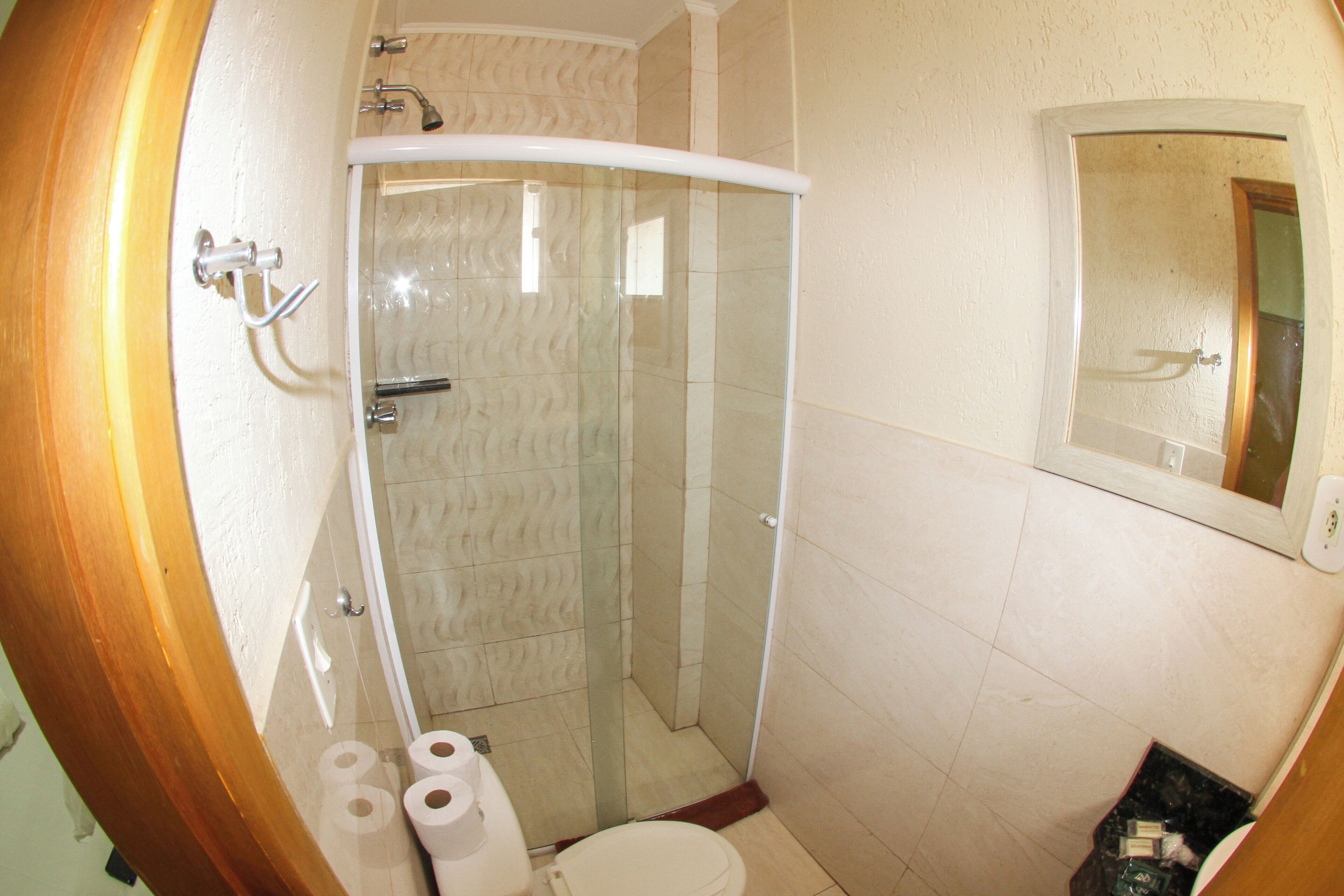 A bathroom with a glass-enclosed shower, a toilet, and a trash bin.