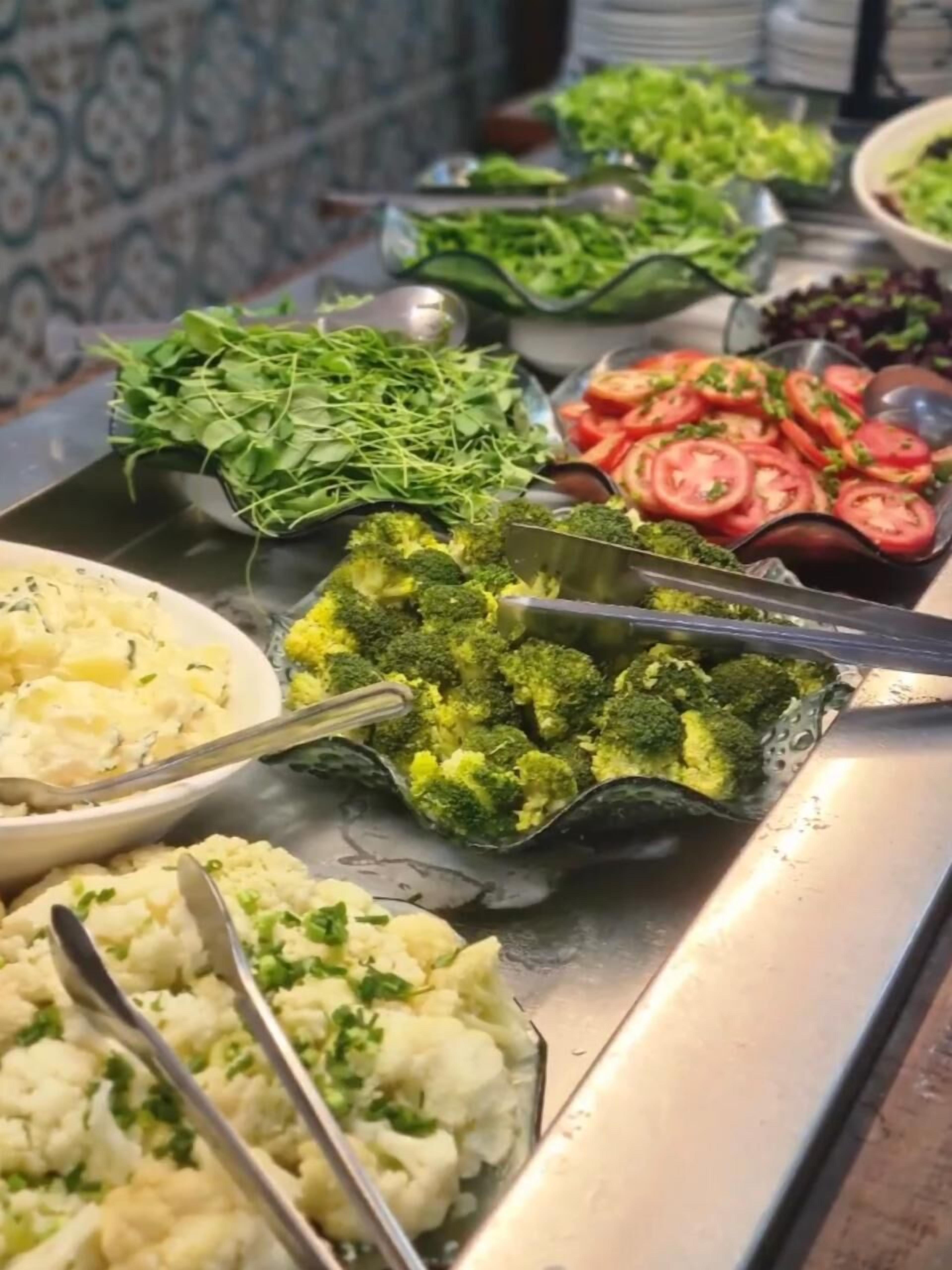 A buffet with various dishes including broccoli, tomatoes, and mashed potatoes.