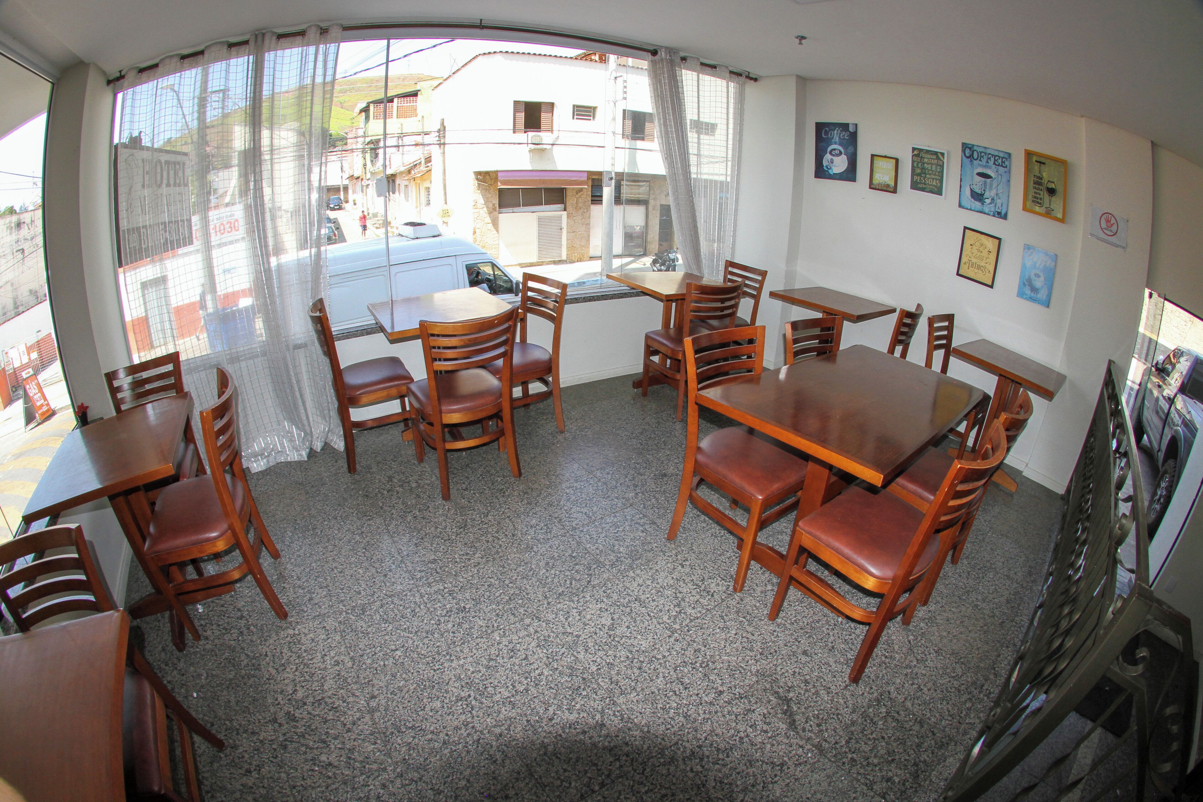 Un comedor con mesas y sillas de madera, una ventana con cortinas y varias fotografías enmarcadas en la pared.