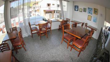 Un comedor con mesas y sillas de madera, una ventana con cortinas y varias fotografías enmarcadas en la pared.