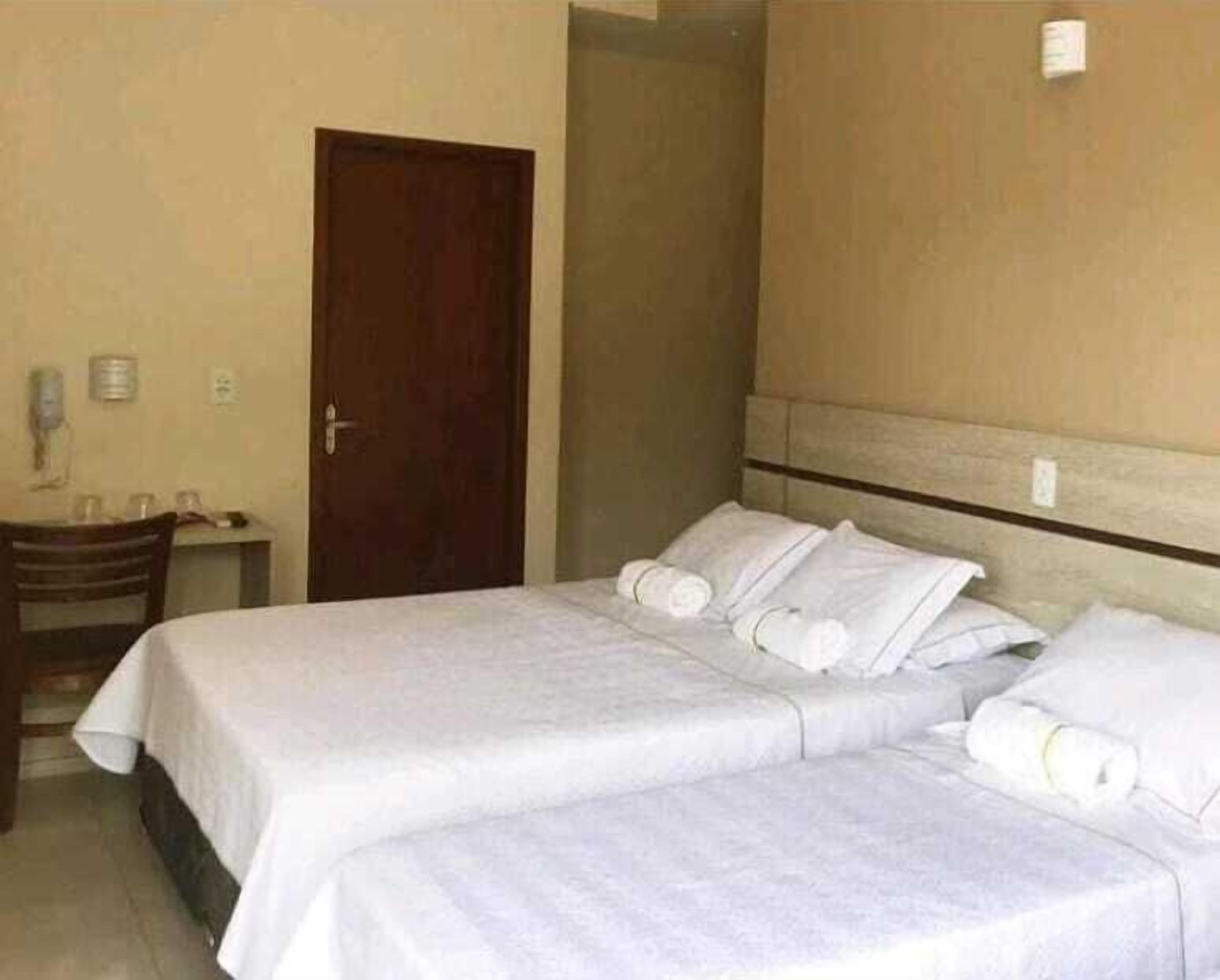 Habitación de hotel con dos camas, una silla de madera, una mesita con un vaso y una puerta.