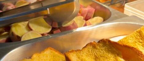 A buffet with various food items including sliced apples, ham, and toast.