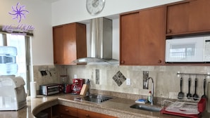 Una cocina con armarios de madera, un lavamanos de acero inoxidable, un microondas, una cafetera y un tostador.