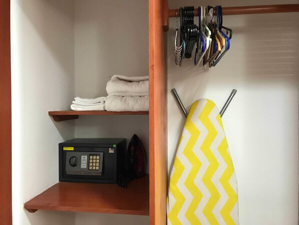 A room with a wooden shelf holding folded towels, a black electronic device, and a yellow and white chevron-patterned item hanging on the wall.