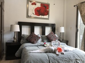 A neatly made bed with a grey duvet, two patterned pillows, and a decorative swan arrangement with flowers. - Lilas del Mar (Playa del Carmen)