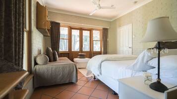 Un dormitorio con cama, una mesita de noche con lámpara, ventana con cortinas, puerta y ventilador de techo.