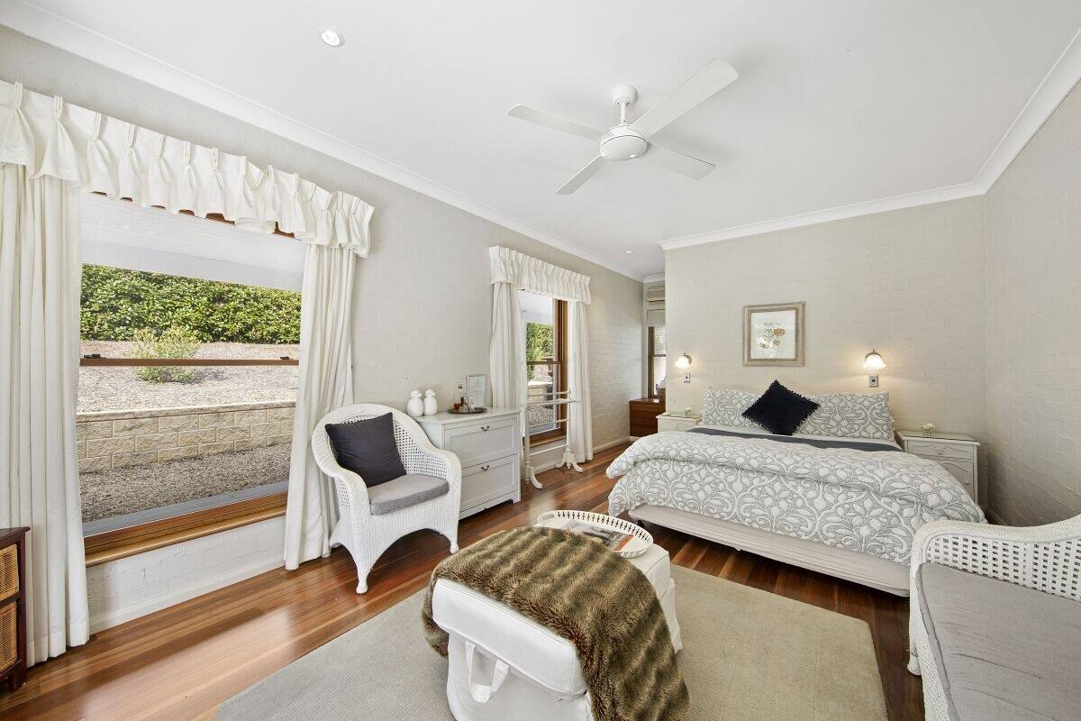 A bedroom with a bed, two nightstands, a dresser, a chair, a window with curtains, and a ceiling fan.