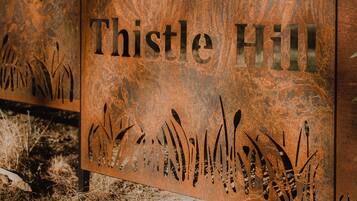 A metal sign with the text "Thistle Hill" and decorative grass patterns.