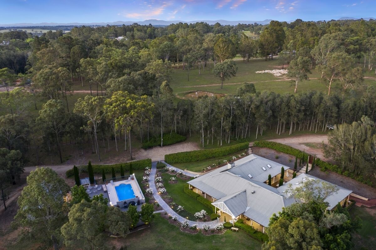 An aerial view of a property with a swimming pool, a large building, and surrounding greenery.