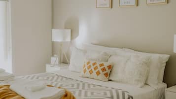 A neatly arranged hotel room with a bed, a bedside table with a lamp, and three framed city maps on the wall.