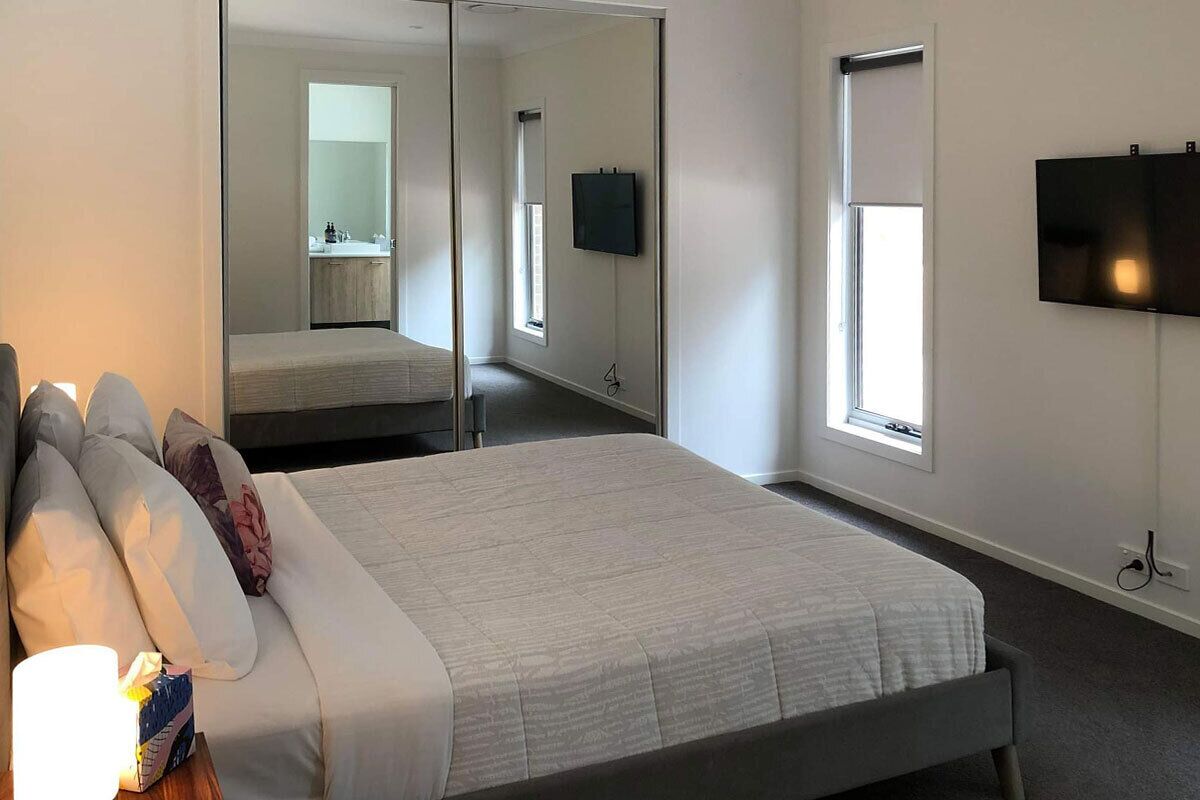 Una habitación de hotel moderna con una cama grande, un televisor de pantalla plana montado en la pared y un espejo amplio que refleja la habitación.