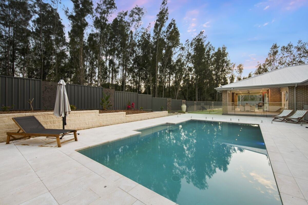 Una piscina rectangular amb una terrassa enrajolada, rodejada de gandules i una zona de porxo coberta.