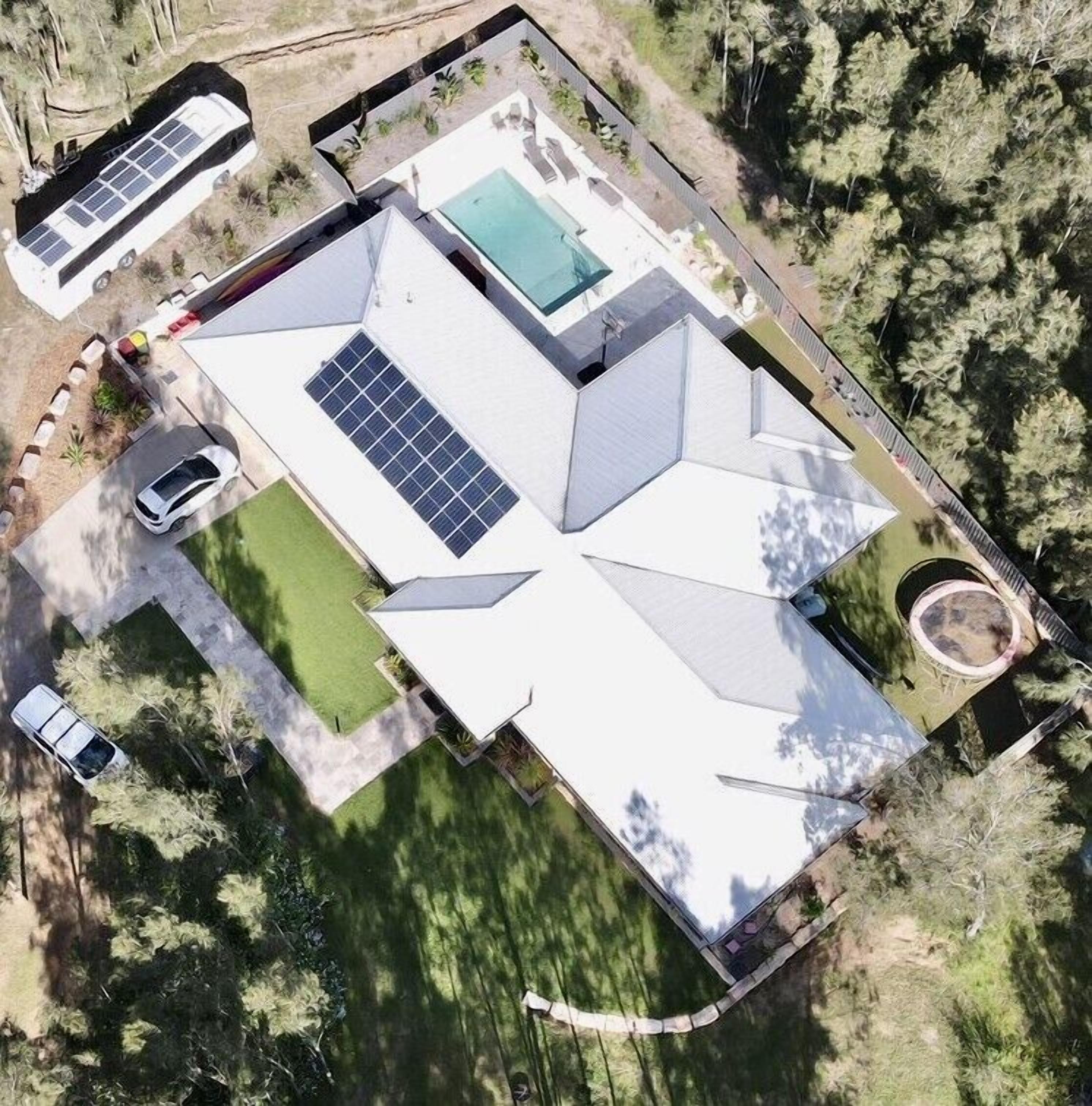 Vue aérienne d’une maison moderne dotée d’une grande piscine, de panneaux solaires et d’une pelouse bien entretenue.