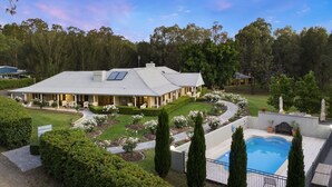 A large house with a swimming pool, surrounded by well-maintained gardens and tall trees. - Thistle Hill Guest House (Pokolbin)